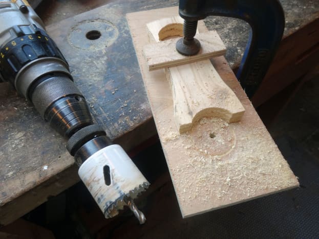 Using sacrificial wood for grip for the drill bit, so as to use a hole cutter saw for creating the curved base of the stand.