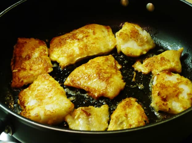 Photo of saut&eacute;ing the lightly battered fillets of fish in a non-stick skillet on top of the stove.
