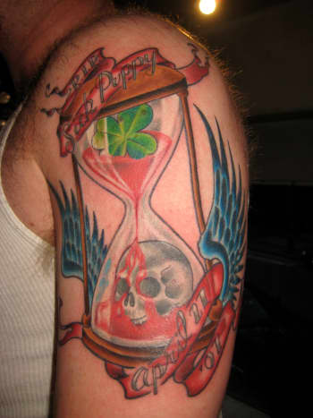 Hourglass tattoo with skull, wings, and shamrock