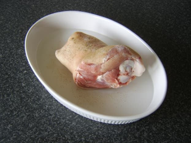 Pork shank is laid on ovenproof tray and seasoned