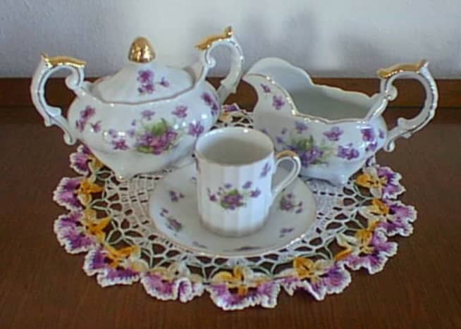 Dainty violet tea set with 22 carat gold trim on hand-crocheted doily
