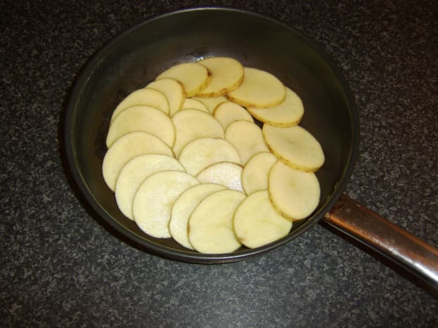 Potato slices are carefully arranged in a deep frying pan