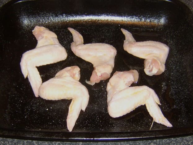 Chicken wings are laid on oiled roasting tray and seasoned