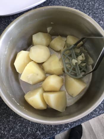 Drained potato pieces are hand mashed