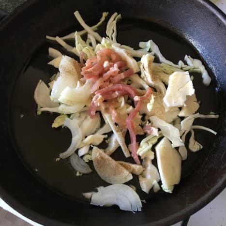 Cabbage, onion and bacon are added to hot pan and seasoned