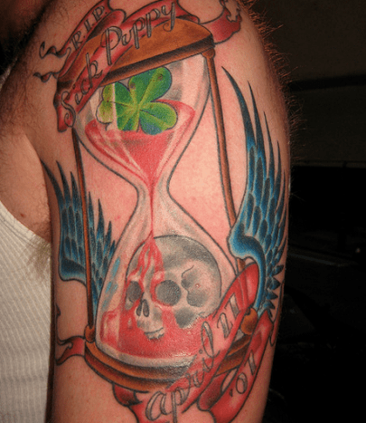 An hourglass tattoo with blood, skull, wings, and four-leaf clover.