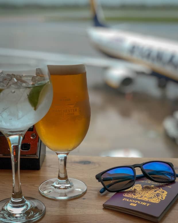 A photo of alcoholic beverages, sunglasses, and a passport in the foreground, with an airplane in the background.