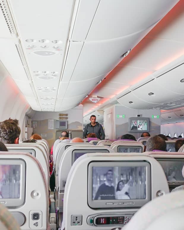An airplane cabin mid-flight, with a man walking down the aisle