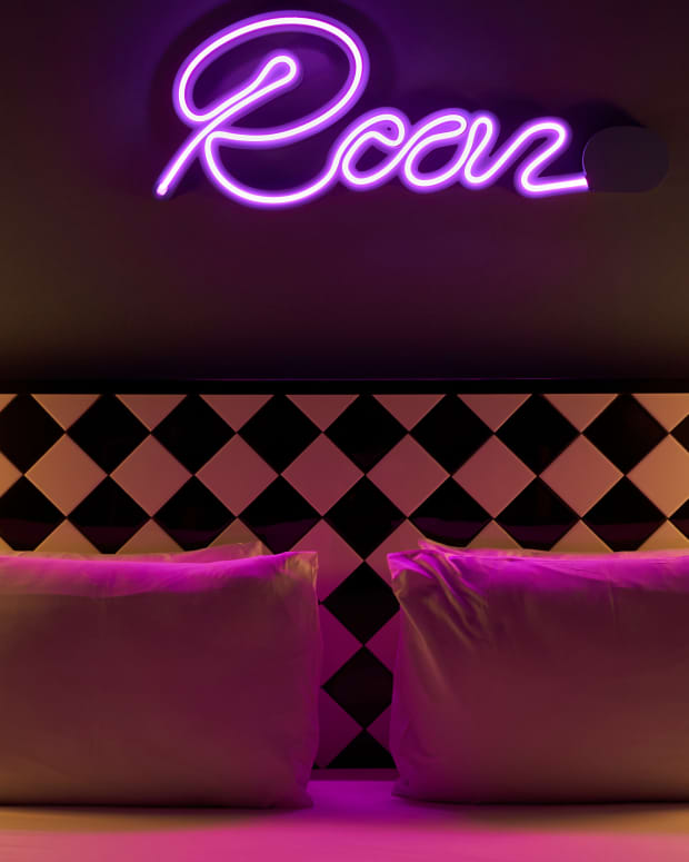 Photo of a bed in an erotic hotel room, with a pink neon sign saying "roar"