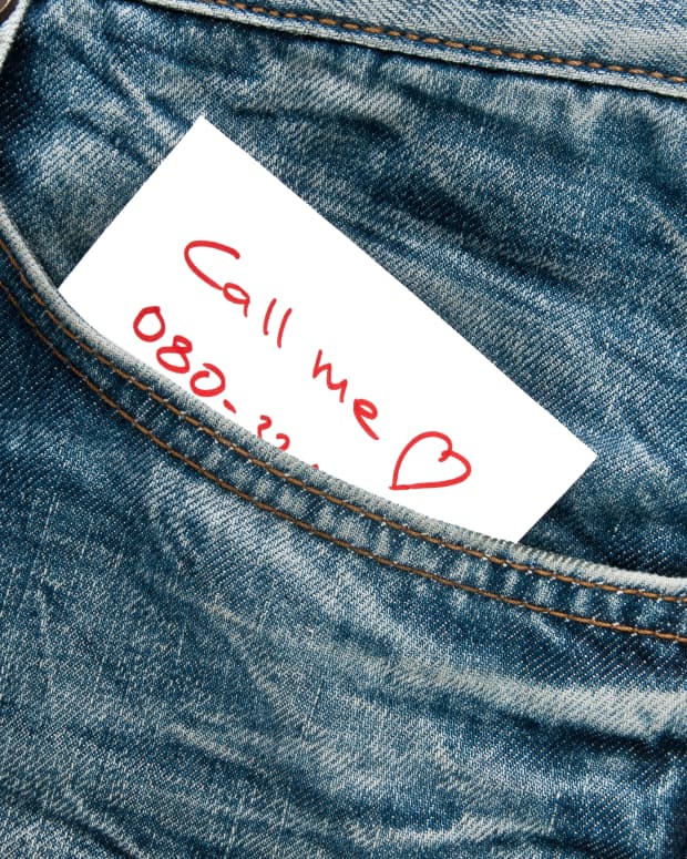 A note sticking out of a jean pocket that reads "call me" with a heart. Part of a phone number is visible.