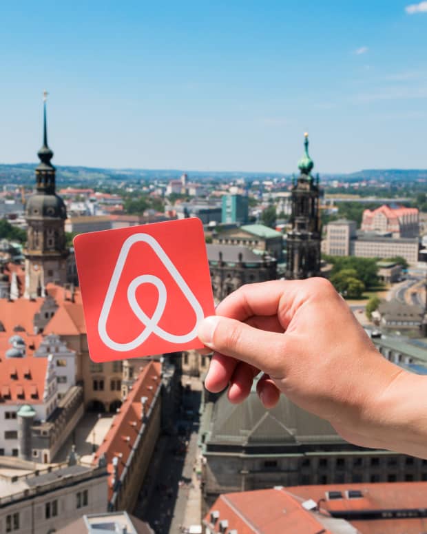 A person holding the Airbnb logo over a high-up view of Dresden, Germany
