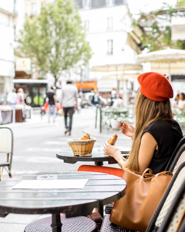 A young woman in a red beret with her back to the camera sits at a Parisian cafe