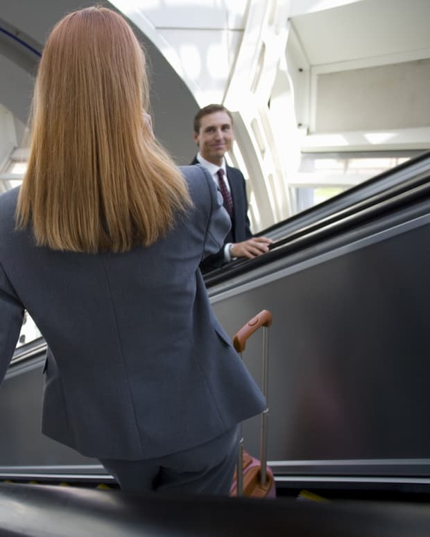 Two travelers share a flirtatious gaze as they pass each other on the airport escalator
