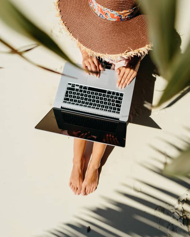Aerial shot through the leaves of a palm tree, of a woman typing on her laptop at the beach