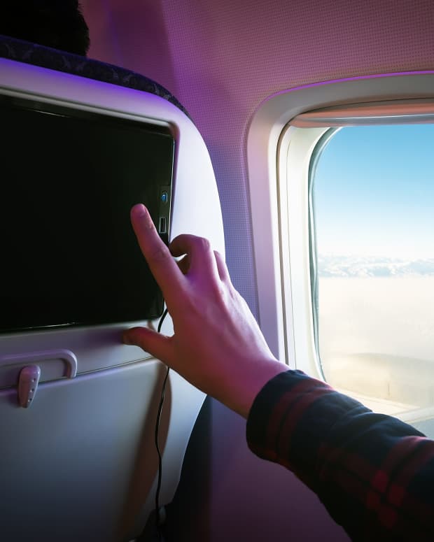 Photo of a hand tapping the in-flight screen of their airplane seat
