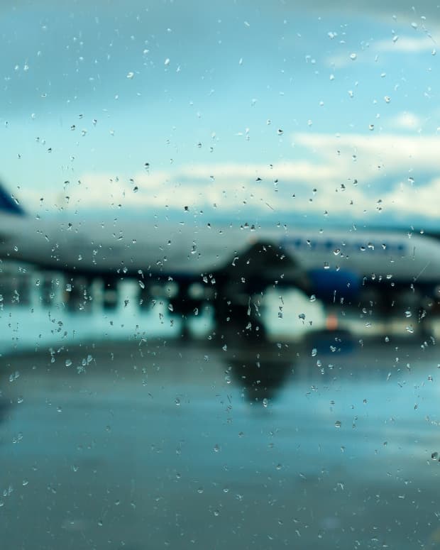 View out of a raindrop-covered window onto a wet tarmac, cloudy sky, and grounded passenger jet plane