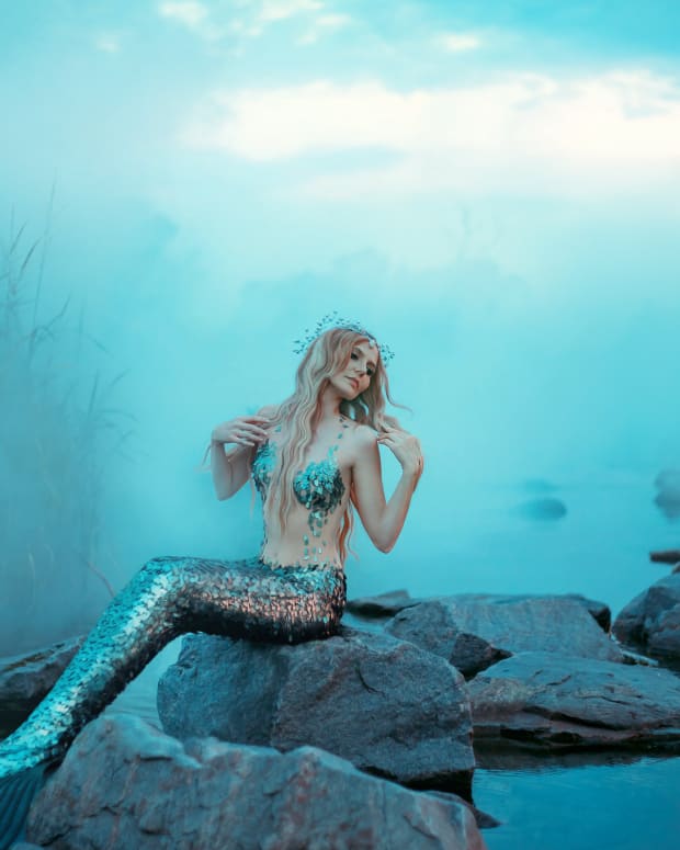 woman dressed as a mermaid sitting on a rock