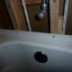 The overflow does not need caulking. Screws fastening the tub can be seen in the lip above the tub, as can the shims between the tub and the stud behind it.