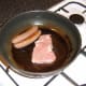 The link sausages and the leg of pork steak are added to the frying pan first