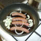 Sliced onion is added to the partly fried sausages