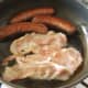 Bacon is added beside the mostly cooked sausages.