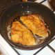 Breaded sea bream fillets are turned in frying pan