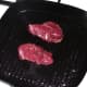 Kangaroo steaks are laid in smoking hot griddle pan