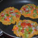 Step three: Heat some oil in a pan. Pour a table spoon batter on the hot pan. Gently spread it a little. Top it with mixed vegetables. Make three such pancakes on the pan.