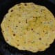 Flip when the bottom turns golden brown. Add a few drops of oil or ghee on the top. Cook the other side until golden brown. Remove and set aside on a plate. Make all the parathas like this.