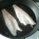 Sea bass fillets are added to the hot frying pan.