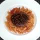 Ostrich burger is laid on spicy pasta bed