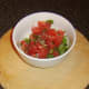 Salsa ingredients are finely chopped and added to a bowl.