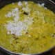 Step six: The bottle gourd and mung beans are almost cooked. Add grated coconut, turmeric powder, jaggery powder, and remaining salt. Mix well. 