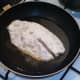 Floured tilapia fillet is laid in medium hot frying pan