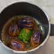 Step five: Heat oil in a cooker base or in a heavy-bottomed pan. Place stuffed brinjal/eggplant one near the other. Cook on low fire for 3 minutes, turning them occasionally to ensure uniform cooking. Add the remaining paste and 1 cup of water.