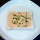 Houmous is spread on bread and garnished with shredded basil