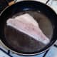 Sea bass fillet is laid in pan to fry