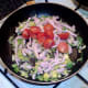 Halved tomatoes are added to sauteed bacon and sprouts