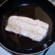 Cod is patted in seasoned flour and added to frying pan