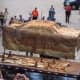 At the convention center, Miss Belvedere is lifted off the 50 year old storage brace that accompanied her in the vault. As they lifted, it became apparent that the bottom of the waterproof plastic bag had rotted away, thus allowing water to seep in.
