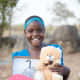 A girl showing off her new stuffed animal and flip flops in Tanzania.