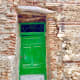 A bright-green, old entrance door to a building where people once lived.