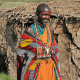 A painted Maasai woman near a Maasai Manyatta (hut) built from dried cattle dung.