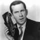 Maxwell Smart, Secret Agent 86 (Don Adams), talking into his shoe phone.  The shoe phone is a series trademark.