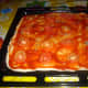 The dough spread with tomato sauce, salt, white pepper, dried oregano, dried basil and topped with round sliced tomatoes.