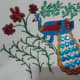 Finish the Madhubani decoration with golden lace for outlining the tail and with blue stones for the feathers. Complete decorating flowers with pearls and stones.