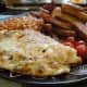 Omelette and chips with baked beans and tomatoes; chips cooked in their skins (potato skins).