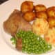 Duck leg is plated with roast potatoes and veg, ready for plum sauce