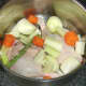 Chopped and prepared vegetables are added to stock pot with duck legs