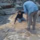 c. On hands and knees to carefully place the unevenly shaped stones.